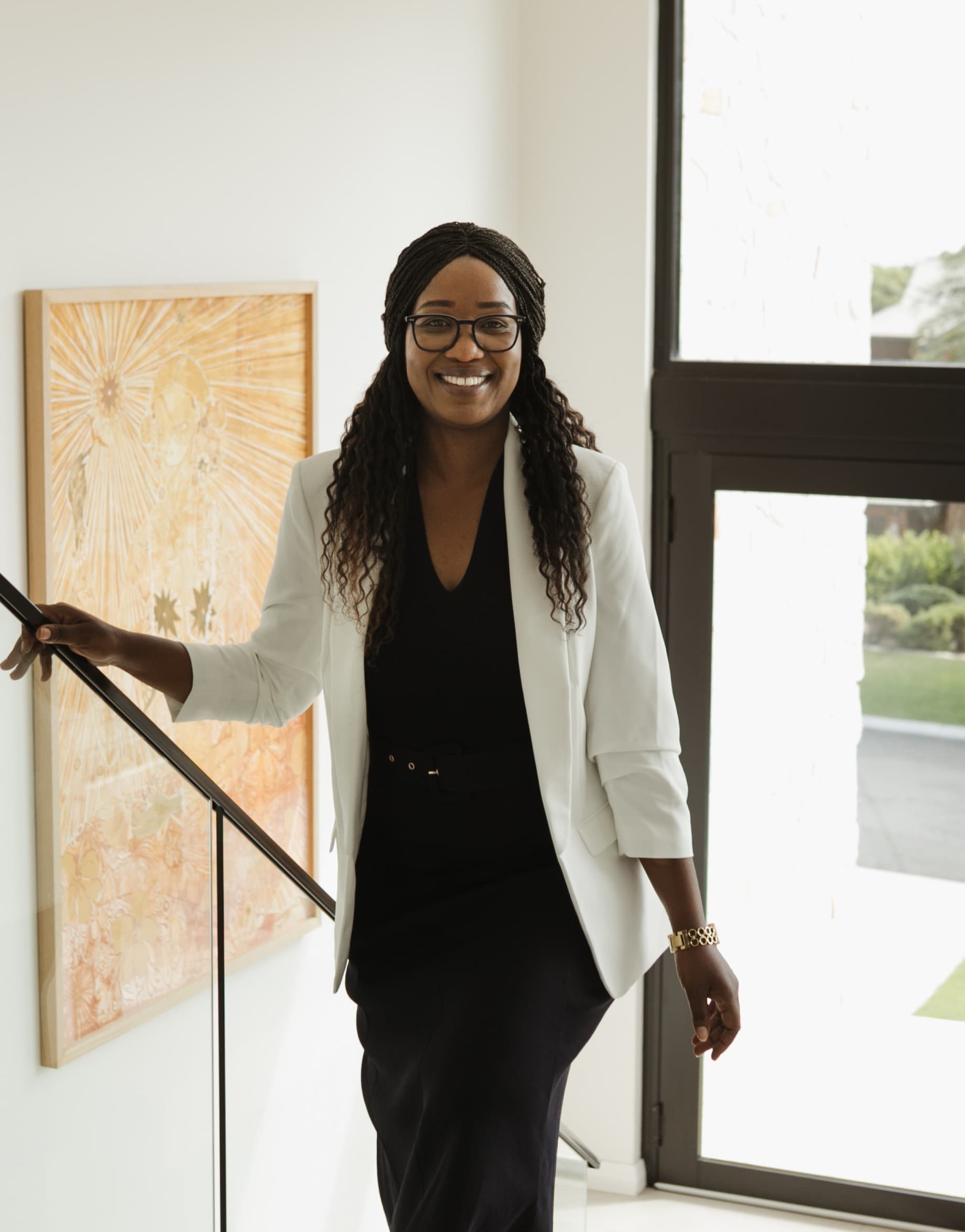 Loveness Matemera, Founder and Buyer's Agent at LBBM Property Group — professional portrait with white blazer holding a laptop in a bright modern office hallway